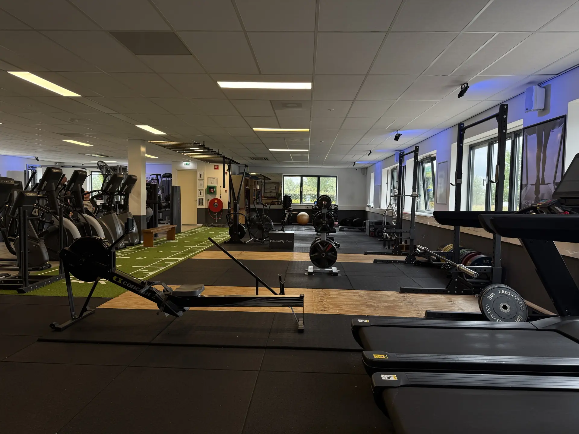 Overzicht van de trainingsvloer met roeitrainers, loopbanden en sledtrack bij Fitcenter Warmenhuizen